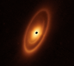 An orange oval extends from the 7 o’clock to 1 o’clock positions. It features a prominent outer ring, a darker gap, an intermediate ring, a narrower dark gap, and a bright inner disk. At the center is a ragged black spot where the detector is saturated.