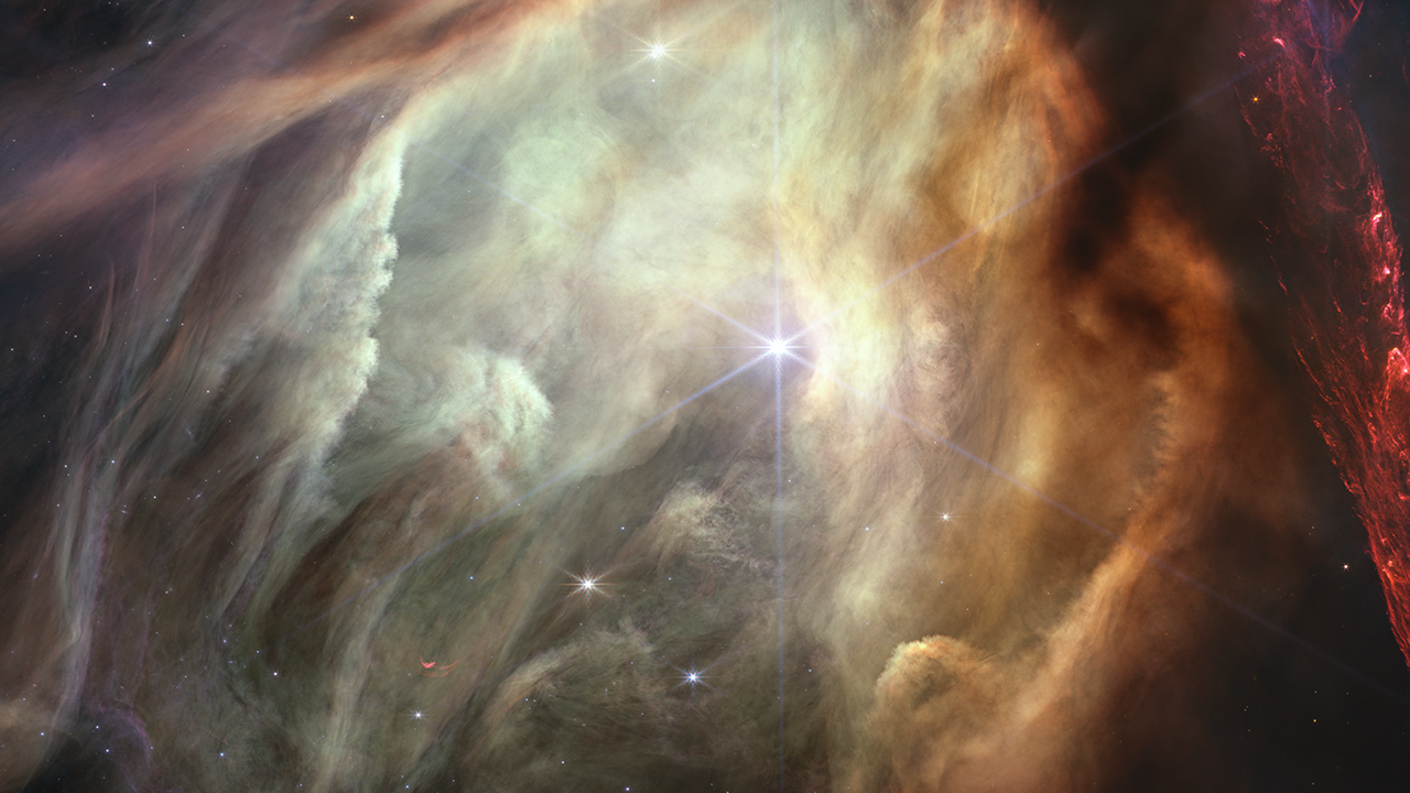 A glowing cave-like structure in shades of yellow, orange, and light green. Vertical curtains of material drape the left side of the image. At right, dark swaths of dust line the edge of the cave. At far right are hints of red.