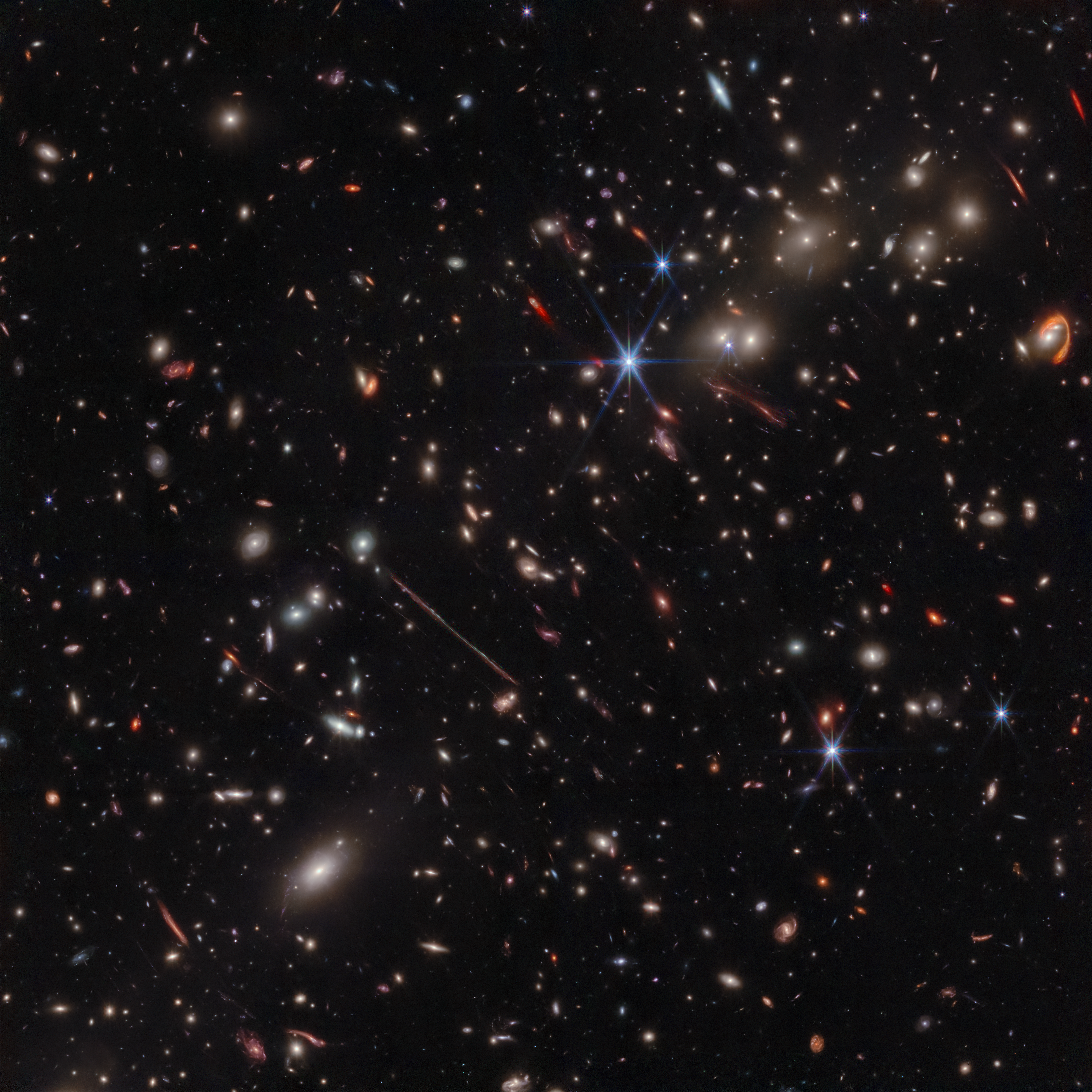 A black background is scattered with hundreds of small galaxies of different shapes, ranging in color from white to yellow to red.