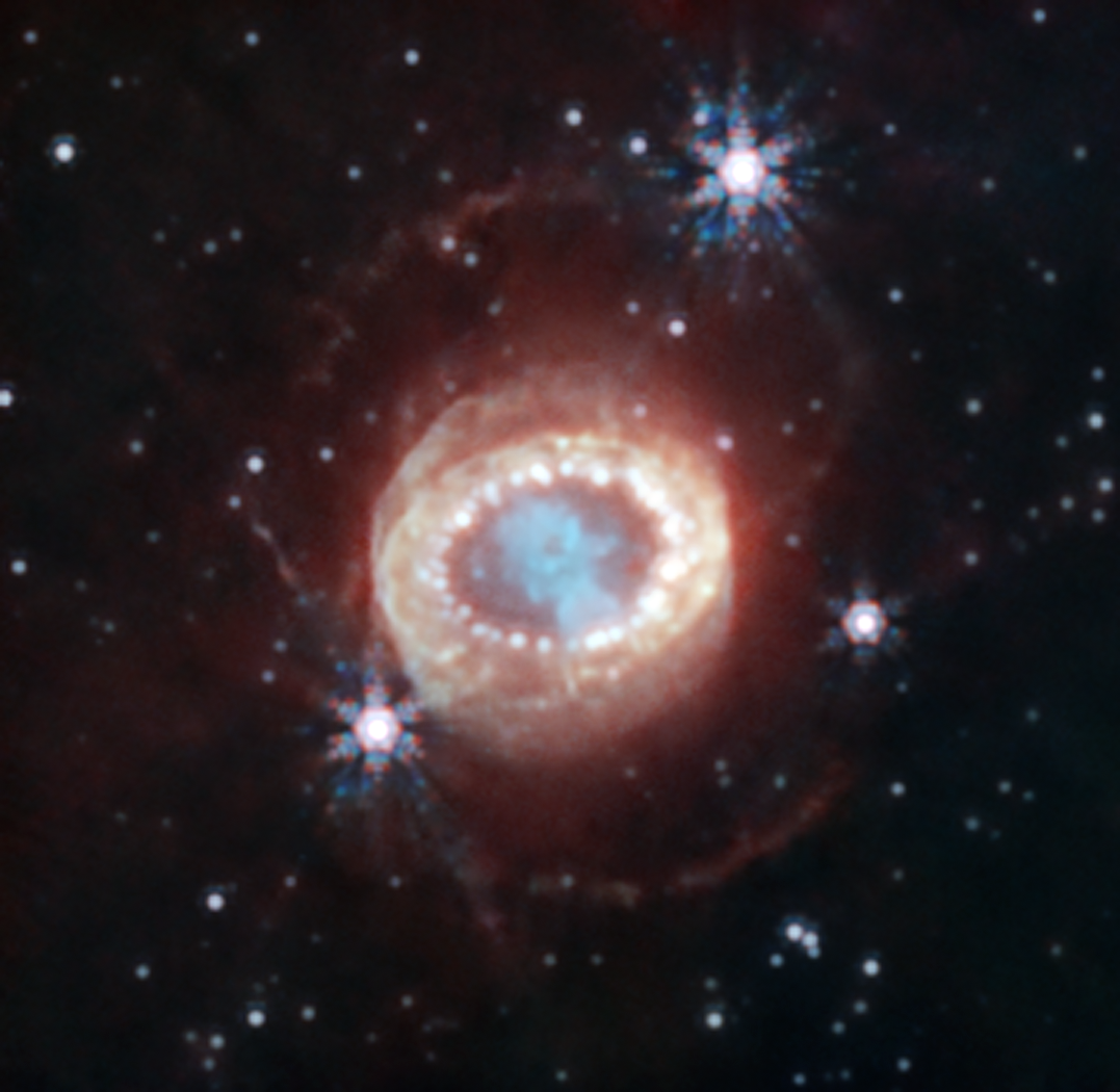 A supernova. The center of the image contains a dense green cloud, shaped like a keyhole. Within this keyhole, there is a dark spot, composed of even denser gas. Outside of this cloud of gas is a ring of dense orange gas and dust that becomes more diffused as it travels further away from the center. The innermost part of this dense orange ring contains brighter orange clumps of glowing gas. Outside of these structures, both above and below them, are very faint orange rings of gas and dust. There are several bright white stars, three of which show an eight-pronged diffraction pattern brought about by the Webb Space Telescope. Several other white stars are strewn throughout the image.