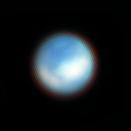 A blue-and-white sphere against a black background is somewhat reminiscent of the famous “Blue Marble” picture of Earth from space. With fuzzy, diffuse edges, this sphere features darker blue patches in most of the northern hemisphere facing the viewer. One, large, crescent-shaped, white patch extends along left side of the southern hemisphere facing the viewer, and a larger, blobby, white patch covers the middle latitudes of the right side of the southern hemisphere. Lighter blue regions border these white patches in the south.