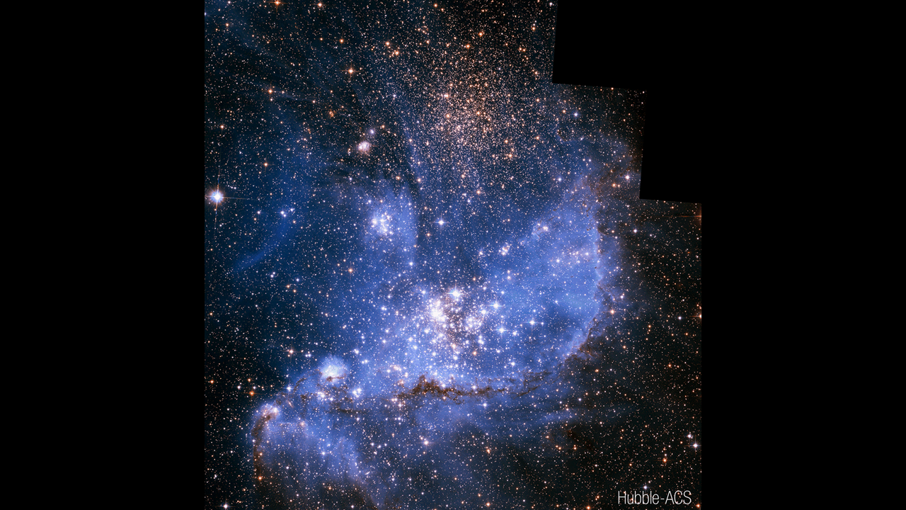 The middle of the image is filled with translucent blue gas that is vaguely boat-shaped, with the tips of the boat at lower left and upper right. A cluster of bright stars is in the middle of the thickest gas, while a smaller cluster is above it. Dark streaks of dust outline the keel of the boat. Thousands of additional stars fill the image, with a particular concentration located at the top center. The image is labeled “Hubble ACS.”
