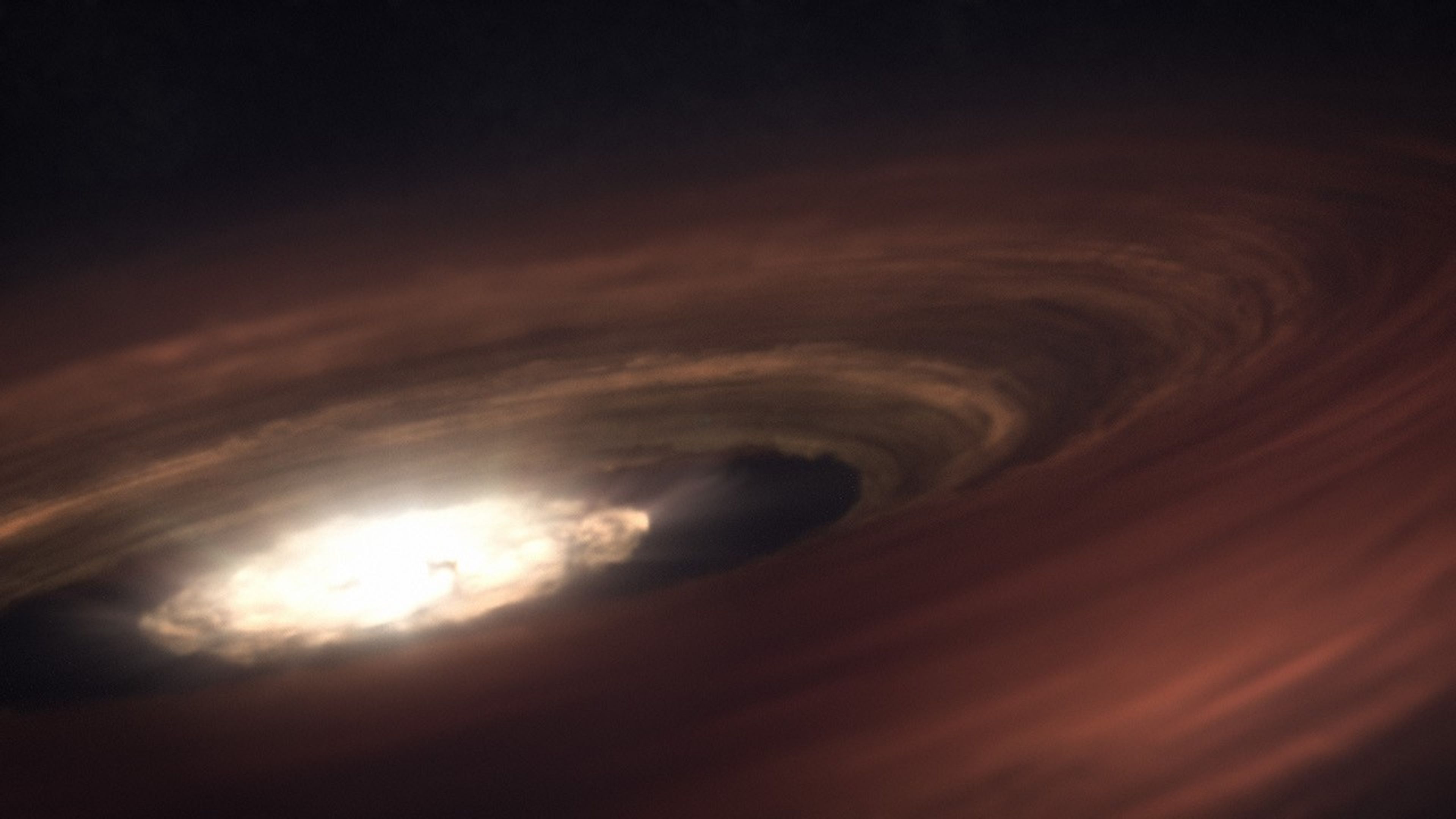 Illustration looking in from the outer edge of a disk surrounding an indistinct bright region. Rays of light emanate from the central area. A dark gap in the disk appears between the bright core and the dusty, hazy outer regions, which build up slightly as you move outward, so that the core appears sunken.