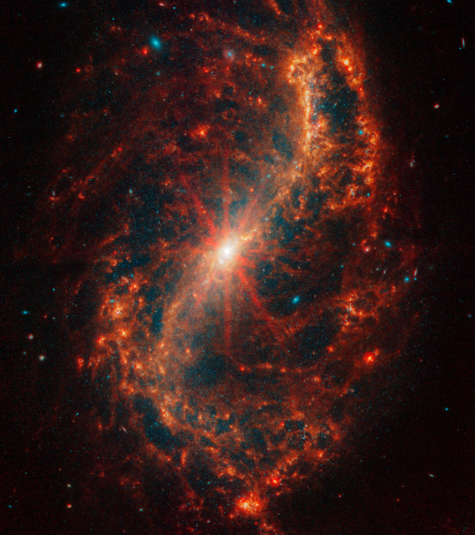 The central core of Webb’s image of the galaxy NGC 7496 begins as a bright white dot that melts into bright oranges. Eight prominent diffraction spikes emanate from the center. A bright orange arc that looks like a thin, backward S forms the bar and two of the face-on spiral galaxy’s arms.