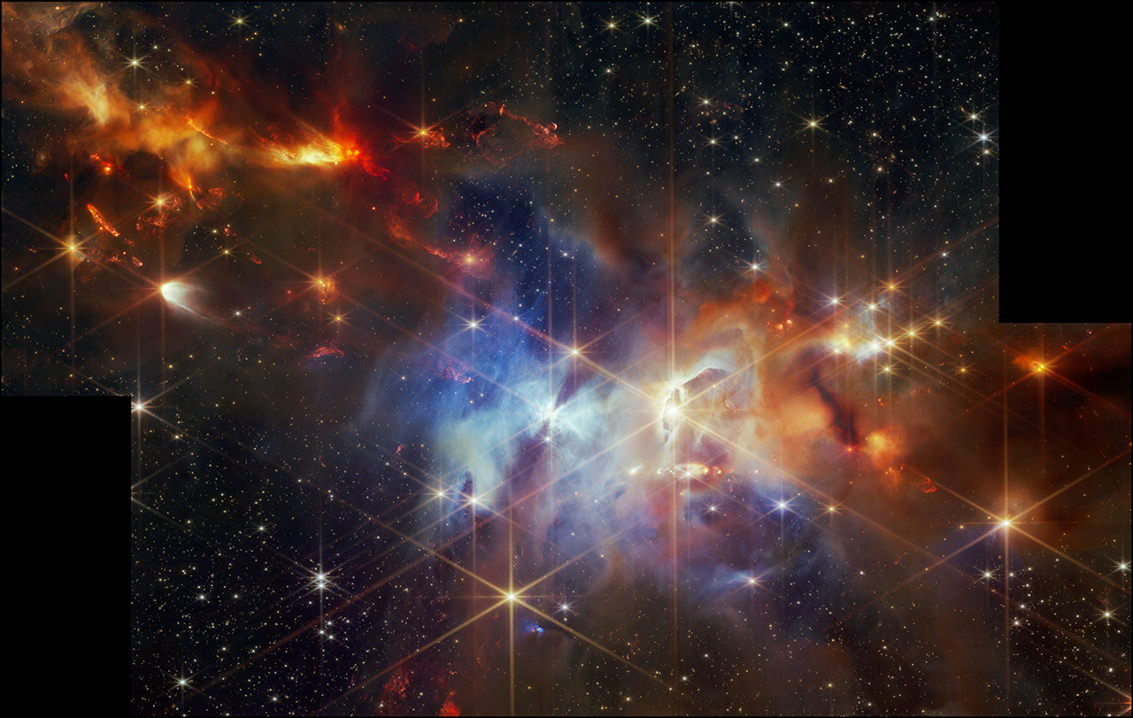 A rectangular image with black vertical rectangles at the bottom left and top right to indicate missing data. A young star-forming region is filled with wispy orange, red, and blue layers of gas and dust. The upper left corner of the image is filled with mostly orange dust, and within that orange dust, there are several small red plumes of gas that extend from the top left to the bottom right, at the same angle. The center of the image is filled with mostly blue gas. At the center, there is one particularly bright star, that has an hourglass shadow above and below it. To the right of that is what looks a vertical eye-shaped crevice with a bright star at the center. The gas to the right of the crevice is a darker orange. Small points of light are sprinkled across the field, brightest sources in the field have extensive eight-pointed diffraction spikes that are characteristic of the Webb Telescope.