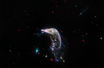 Two interacting galaxies known as Arp 142 in a horizontal image taken in mid-infrared light. At left is NGC 2937, which looks like a tiny teal oval and is nicknamed the Egg. At right is NGC 2936, nicknamed the Penguin, which is significantly larger and looks like a bird with a fanned tail.