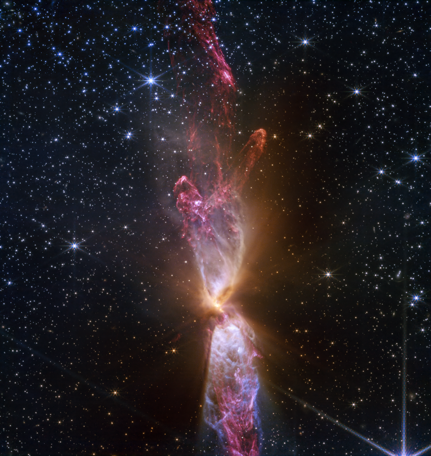 At the center is a thin vertical cloud known as Lynds 483 (L483) that is roughly shaped like an hourglass with irregular edges. The lower lobe is slightly cut off. The top lobe is seen in full, petering out at the top.