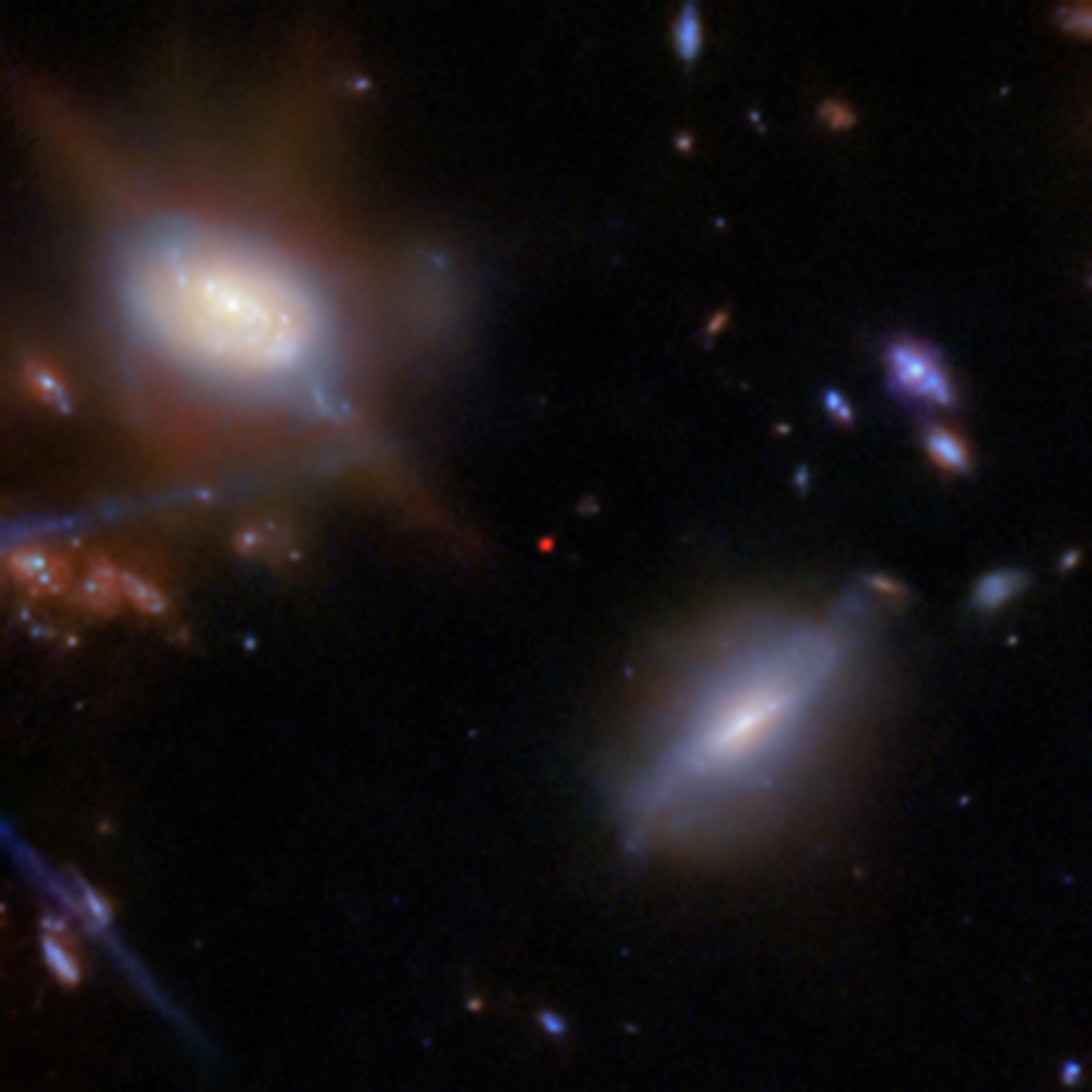 A small red dot is in the middle of the image. To its upper left is a face-on spiral galaxy, and to its lower right is an edge-on spiral galaxy. A handful of other small background galaxies are seen against the black background of space.