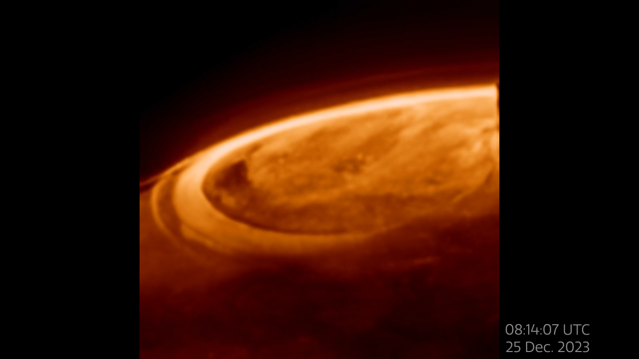 The top of Jupiter in shades of orange. A bright ribbon wraps around the planet's pole. Inside the circle formed by the ribbon is a more mottled area. Below the ribbon, the planet is much darker. A label at right reads 08 14 07 UTC 25 December 2023.