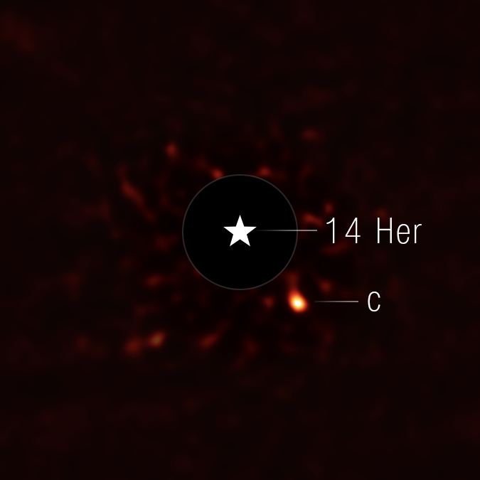 This image shows the exoplanet 14 Herculis c. The view is mostly black, with very faint red splotches in the central region of the image. At the center of the image, there is a black circle, and in the center of that, there is a star symbol representing a real star. This black circle blocks the light from the host star. To the lower right of the circle is a fuzzy bright orange circle, which is the exoplanet.