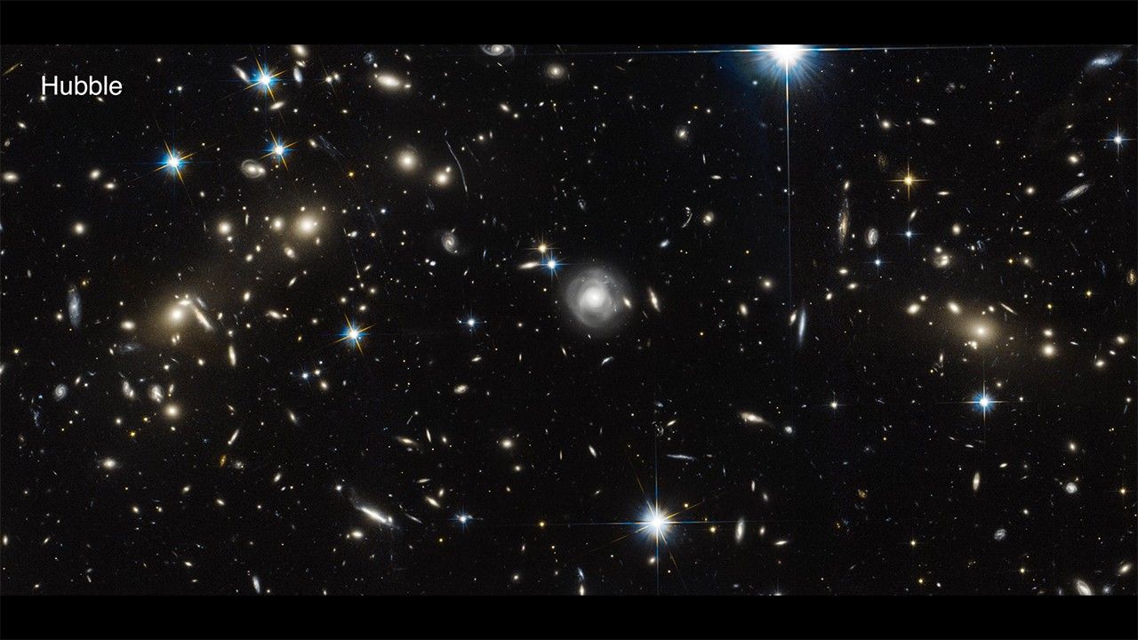 Hubble observation of the Bullet Cluster shows many overlapping objects, including foreground stars, galaxies in galaxy clusters, and distorted background galaxies behind the galaxy clusters. The objects are all at various distances set against the black background of space.