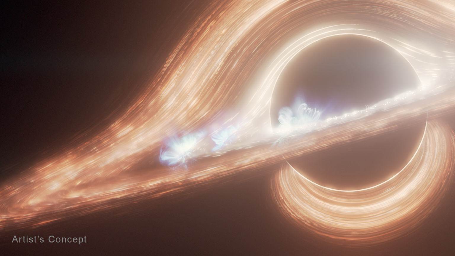 A large, black circle representing a black hole occupies the right third of the frame in this illustration. Thick, clumpy orange streaks arc above and below it, essentially surrounding it. The top arc extends down to the lower left and then curves around in front of the black hole to form a disk that is tilted toward the viewer. Near the inner edge of the disk, several bright, whiter spots have blue filaments looping above them, representing flares. The words “Artist’s Concept” appear in the bottom left corner in gray.