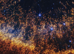A closeup of a small section of the Helix Nebula, an expanding shell of gas and dust. Thousands of orange and gold comet-like pillars stream upward from the bottom, like thin liquid blown up a sheet of glass. These pillars are around the circumference of the arced shell, which forms a partial orange semi-circle at the bottom. The pillars are more numerous and denser at the bottom, and darker red. They fade to orange and then yellow in the arc. In the top two-thirds, they are thinner and more golden, and itu2019s easier to see the black background of space. Several bright blue stars, some with diffraction spikes, are scattered throughout. A few larger stars are on the right side.