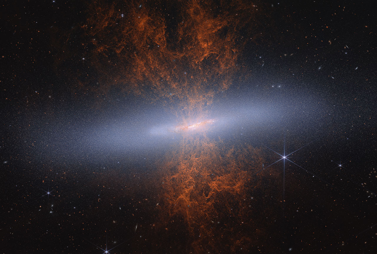 Edge-on spiral starburst galaxy Messier 82 as imaged by NASA's James Webb Space Telescope. Hourglass-shaped red-orange plumes of material are shooting outward from above and below a bright blue-white, disk-shaped center. Messier 82 is set against the black background of space, which has many distant galaxies that appear as small white and orange spirals, ovals, and points of light. Toward the right of Messier 82 is a blue-white star with eight-pointed diffraction spikes that are characteristic of Webb.