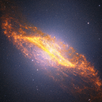 A diagonal image of the galaxy Centaurus A stretches from the upper left to the lower right against a deep black background filled with countless tiny orange, blue, and white points of light. The galaxy is brightest at its center with a white glowing core. A broad band of golden-orange dust cuts across the middle of the galaxy, forming a distinctive parallelogram shape. The dust in this feature is richly textured, with mottled patches, bright knots, and intricate filaments throughout. Just above the center, delicate peach-colored ribbons trace an S-shaped structure. Rather than appearing smooth, the galaxy has a finely speckled texture created by millions of individually resolved stars, which fill the central regions and extend into the surrounding glow. The galaxyu2019s outer edges are reddish-orange and dissolve into diffuse, cloud-like plumes with feathery textures that stretch beyond the dust lane. Against the surrounding darkness, several bright foreground stars display Webbu2019s distinctive diffraction spikes.