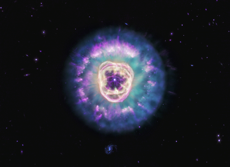 Planetary nebula NGC 2392, also called the Lion Nebula, against the black background of space. The nebula is in the center, circular in shape, and looks like a male lion’s head. In the very center is a small, bluish-white circle with eight-point diffraction spikes, a white dwarf star. Surrounding the star are light purple-red cavernous bubbles and shell-like rings. The bubbles and shells collectively form an oval with two small, wide arcs near the top, reminiscent of a lion’s face and its ears. What appears to be extended outward from the lion’s face is a thick ring of cyan material. The width of the ring is consistent throughout and resembles a mane. The area closest to the lion’s face looks cloudy, while the edges of the mane look like there are purple clumps of dust with comet-like tails and strands. In the background are distant galaxies and stars. Some galaxies appear as small purple points of light and others with visible blue spiral structures. A couple of the stars have diffraction spikes.