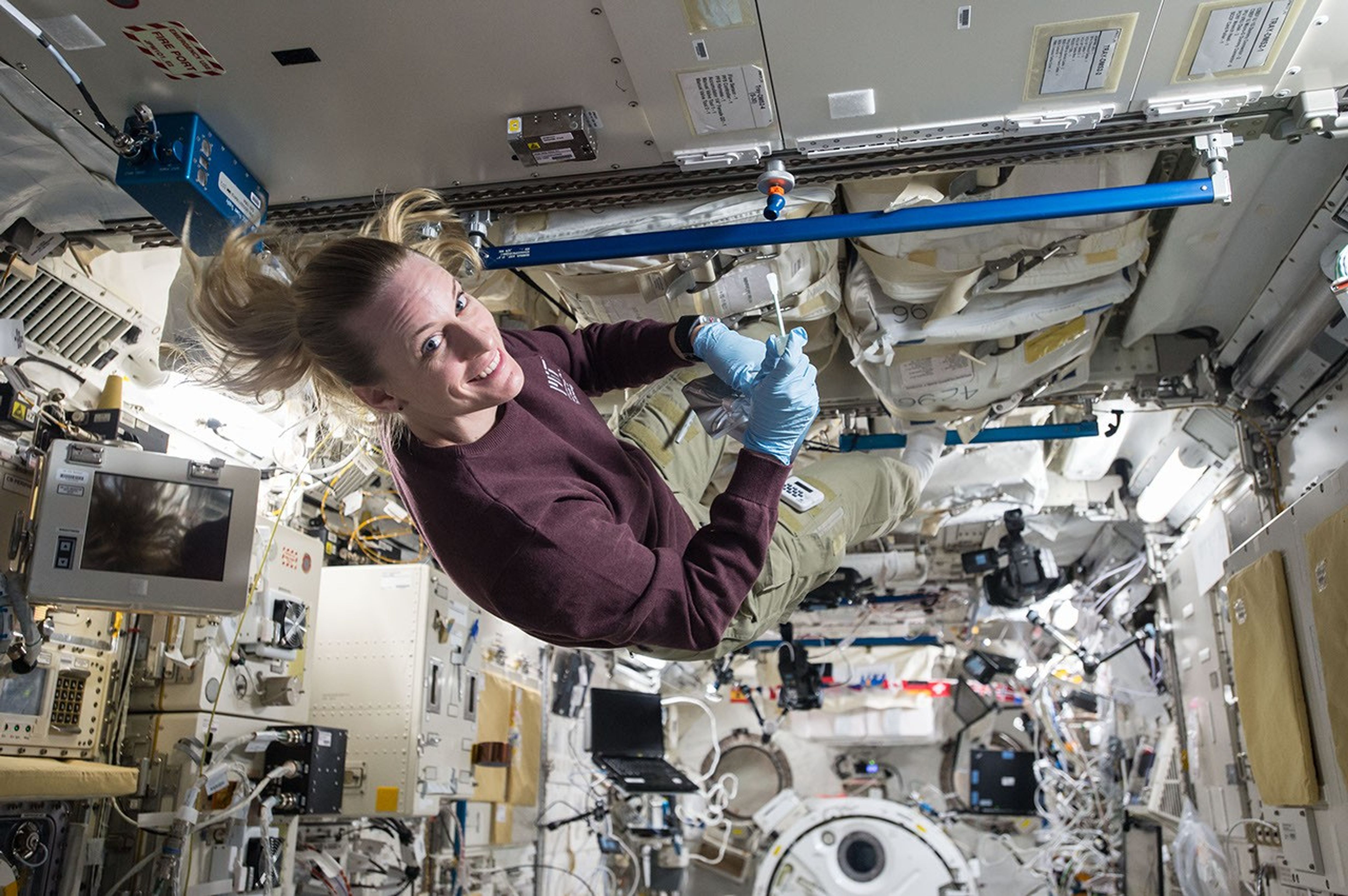 Astronaut conducts scientific work aboard the International Space Station, floating in microgravity surrounded by equipment and research tools.