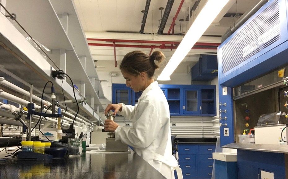 Woman in a science lab holding a metal cylinder.