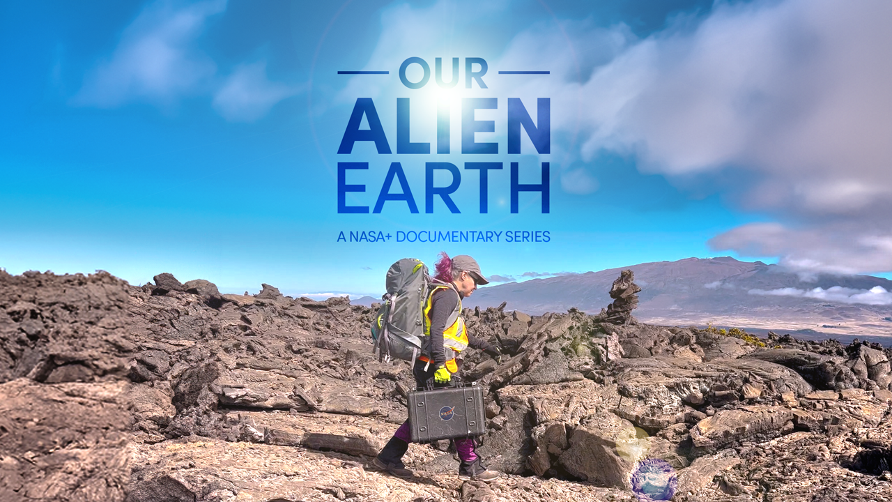 Field scientist carrying a backpack and eqipment case and walking on rocky terrain without apparent vegetation.