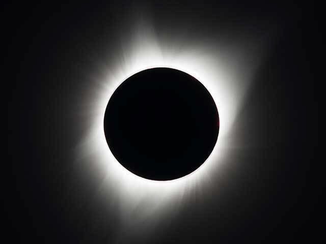 A black circle surrounded by a white, smudgey, streaky halo showing the Moon blocking the Sun during an eclipse.