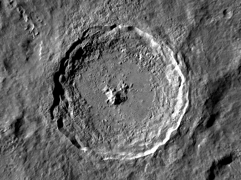 Highly textured crater with a steep-looking rim and a cluster of mountains at its center.
