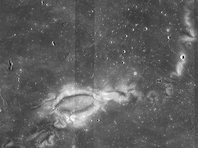 Lunar surface, pockmarked with craters, and dominated by a large, bright, swirl-detailed feature in roughly the shape of a tadpole with a curved tail.