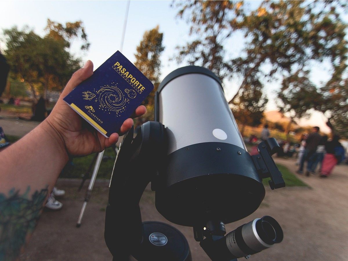 Hand holding a passport next to a telescope.