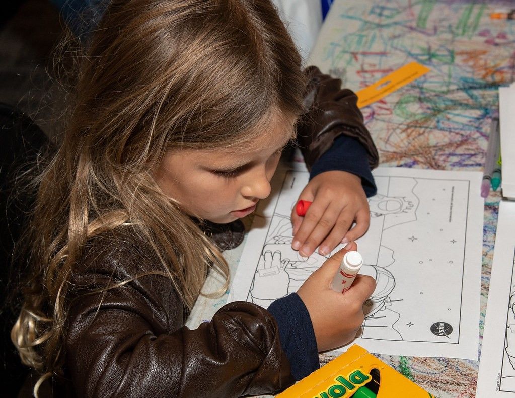 Child coloring a space exploration scene with markers.