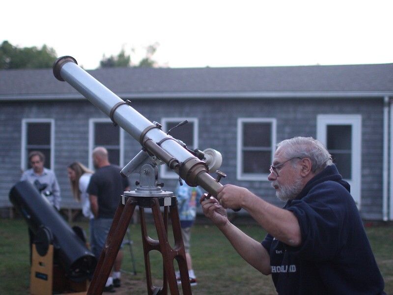 A man adjusting a telescope outdoors.