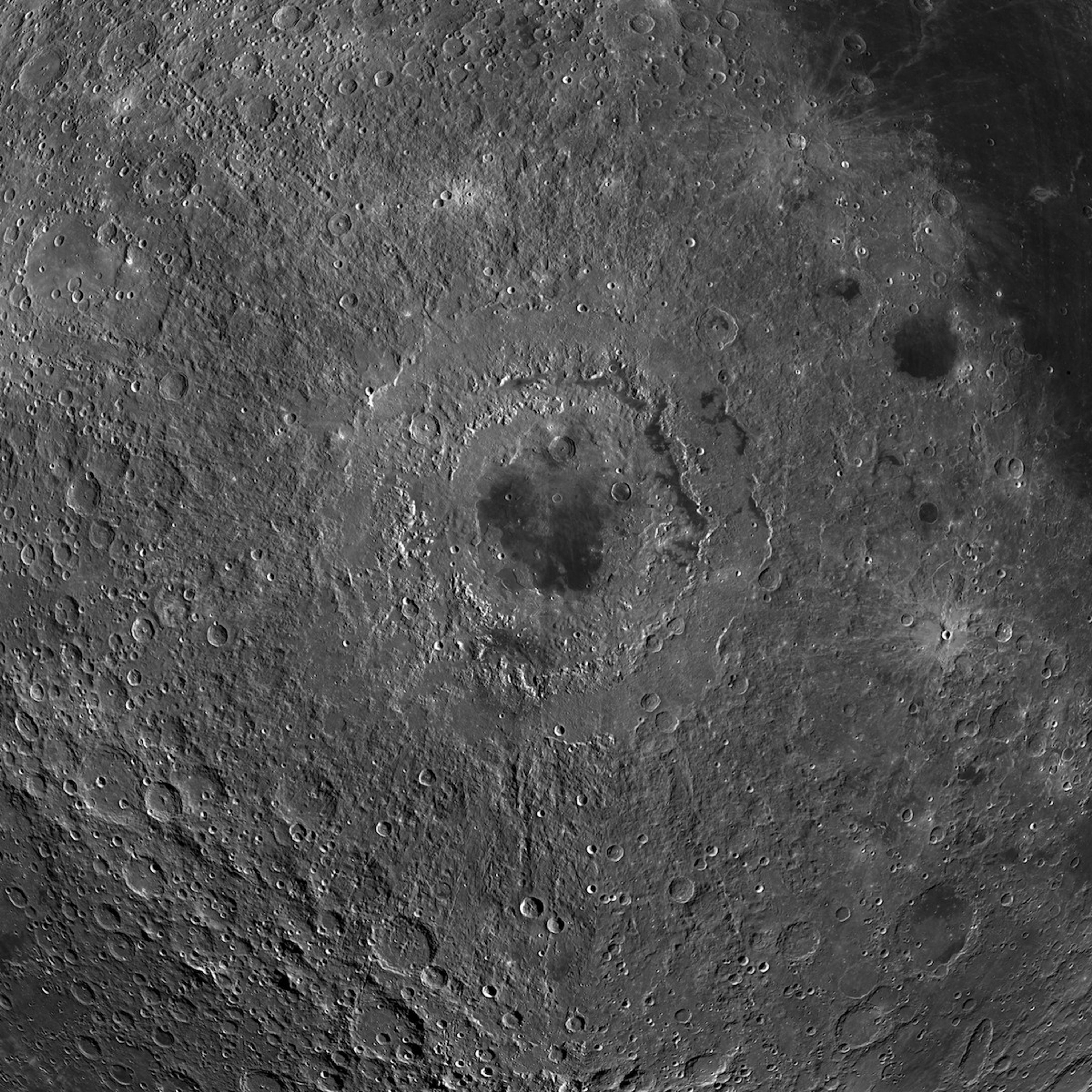Detailed view of lunar surface with many craters. In the center, a large crater has a dark, patchy floor.