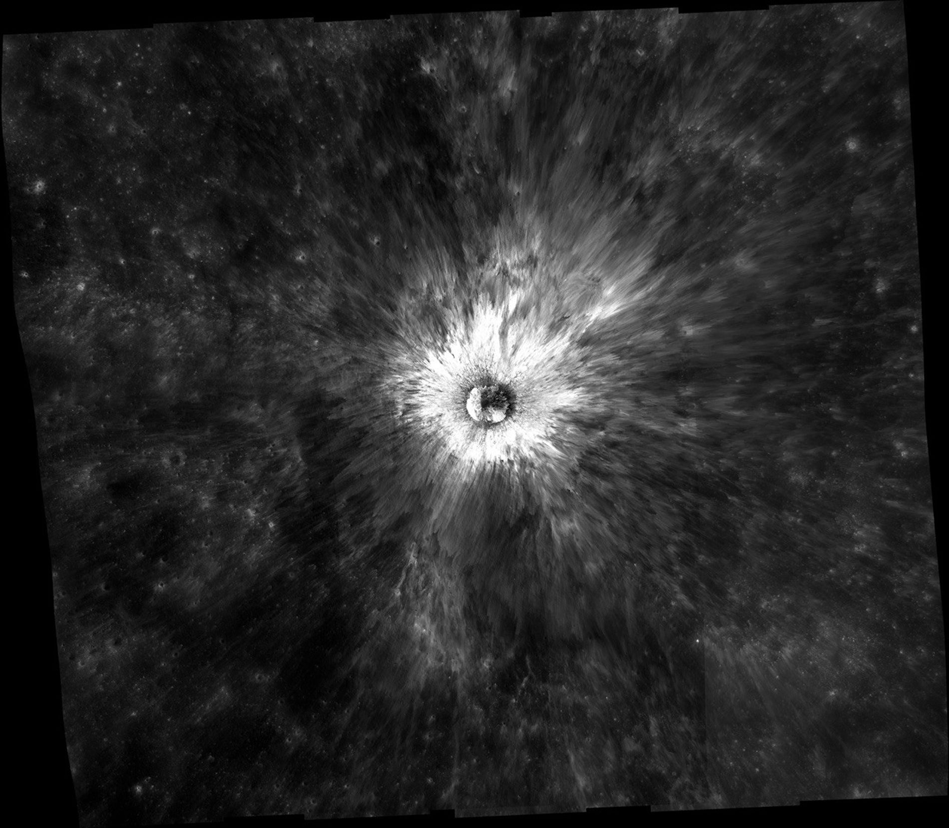 Striking image of a crater on the Moon. Bright white rays spread out from a circle in the middle over a dark gray background.