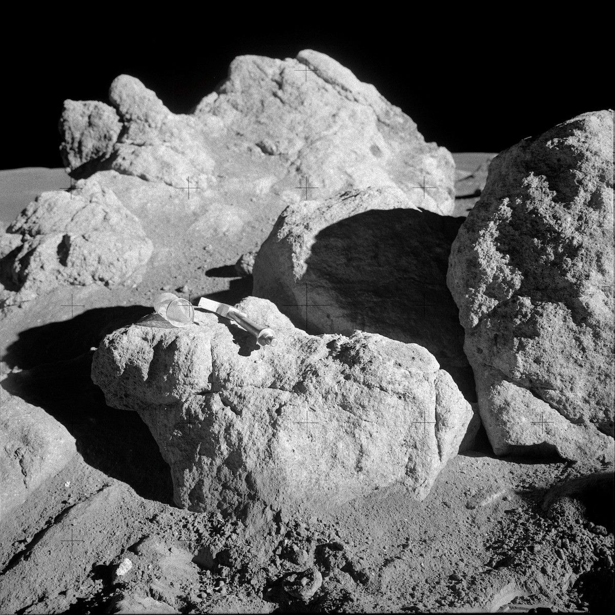 large, white, broken boulder with geologist hammer (much smaller than the boulder) for scale
