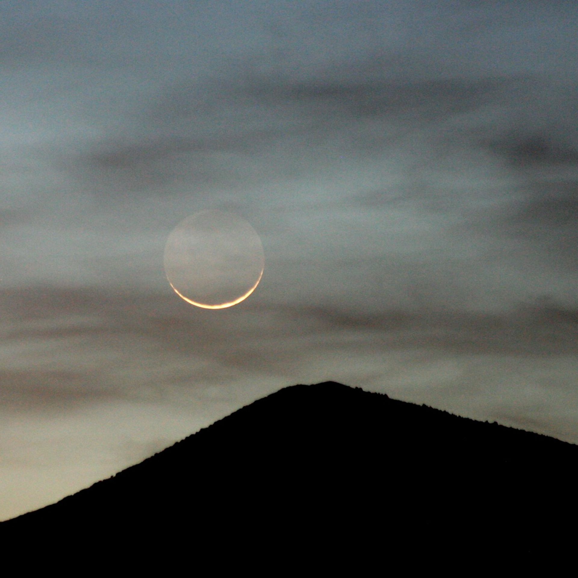 Moon and thin clouds above a single mountain summit