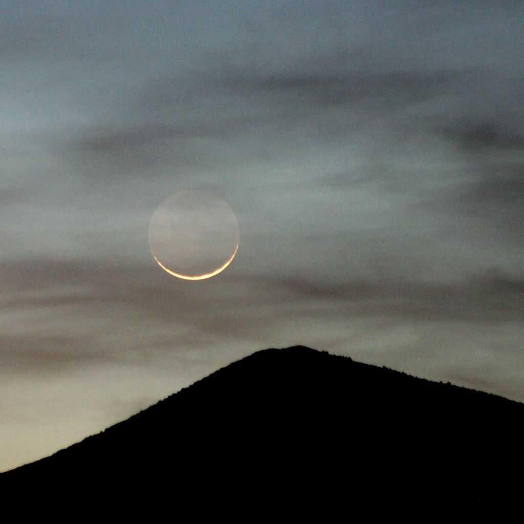 Moon and thin clouds above a single mountain summit
