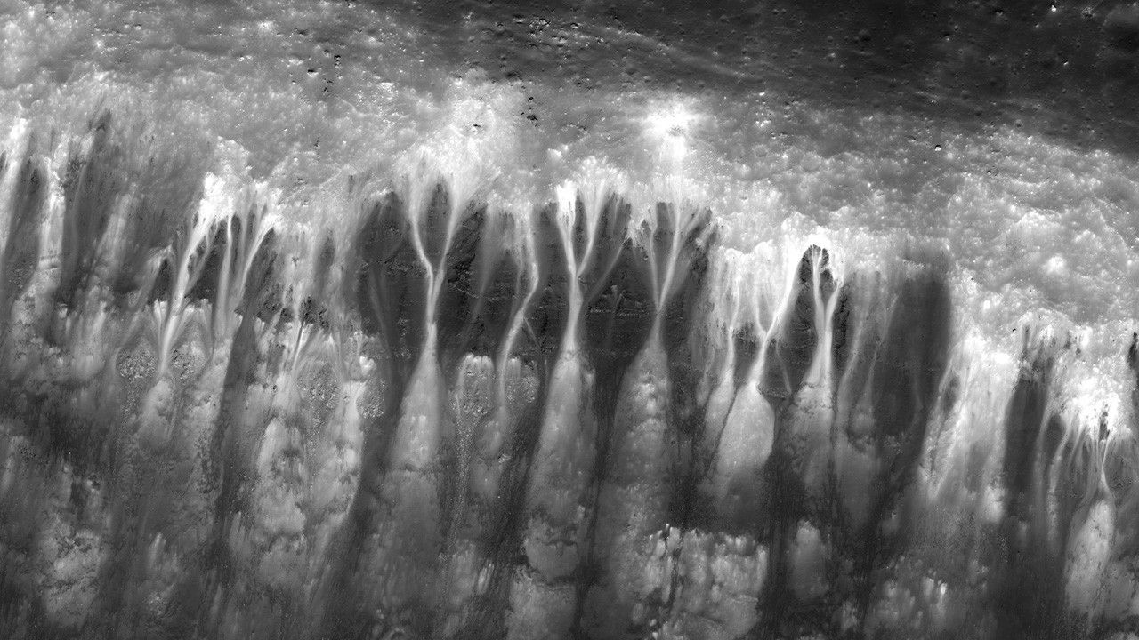 Close-up of crater rim terrain, with stark dark-and-light contrasting streaks resembling trickling patterns.