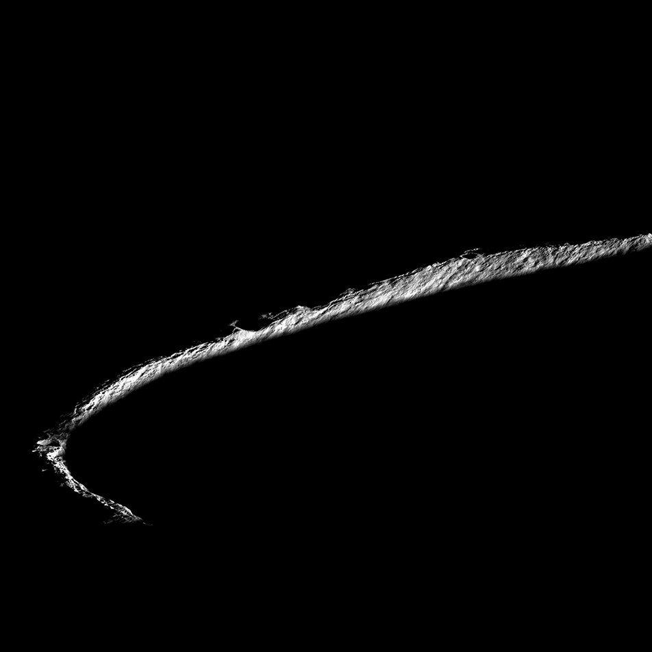 This is an image of Shackleton Crater, an impact crater that lies at the lunar South Pole. The image is engulfed in a sea of darkness, only a sliver of the crater’s rim is illuminated, forming a lit-up half circle. While peaks along the crater's rim are exposed to almost continual sunlight, the interior is perpetually in shadow.