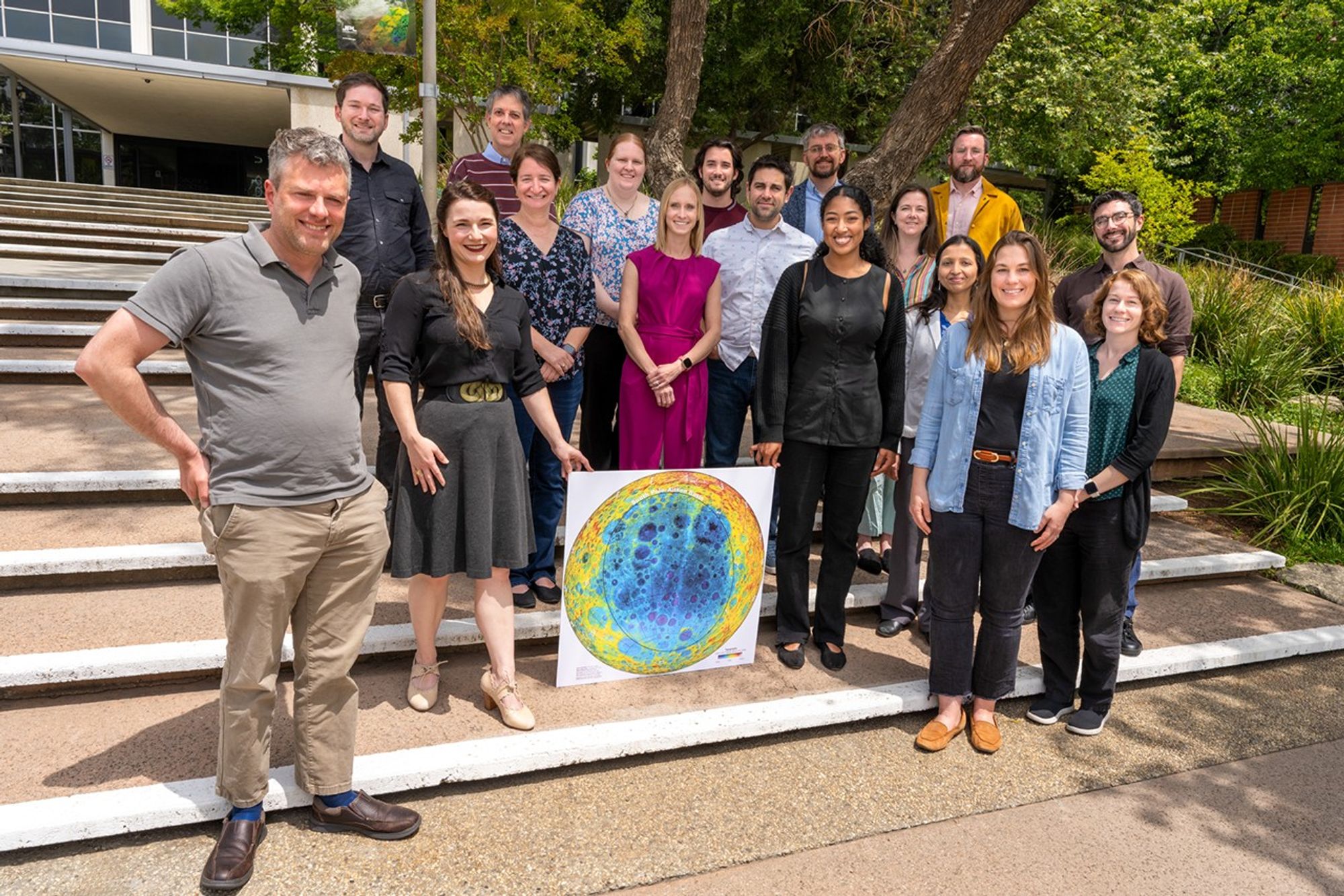 17 members of the SPARX Science Definition Team stand together on steps, around a large printout topographical photo of the lunar surface.