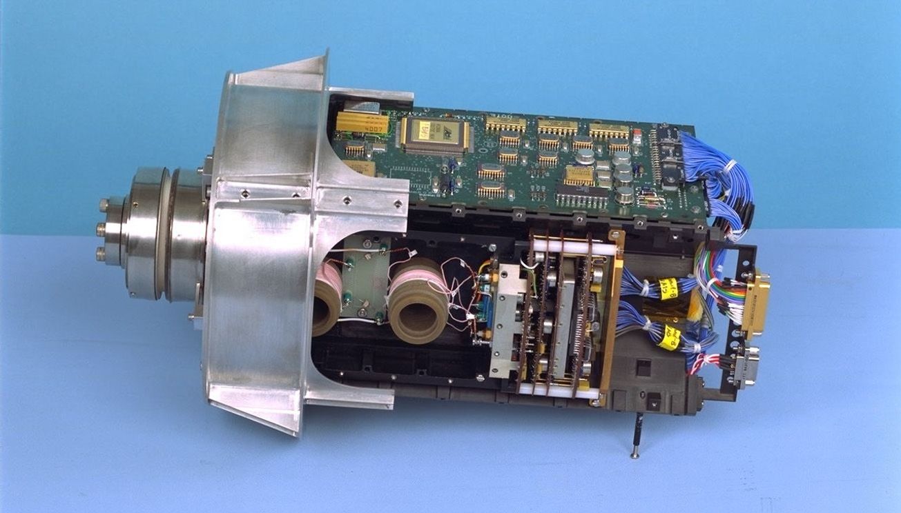A close up photo of a small device with electronic parts assembled in a rectangular block, and topped with a small metallic cylindrical protector.