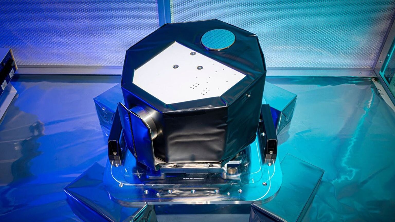 A well-lit laboratory photo of a small covered octogonal instrument situated on a mounting plate.