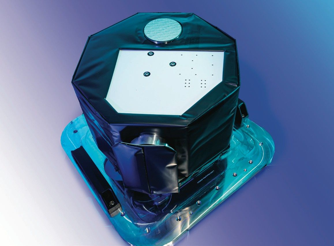 A well-lit laboratory photo of a small covered octogonal instrument situated on a mounting plate.