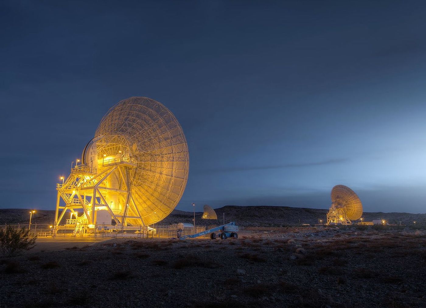 Two giant antennas, illuminated by lights, stand out against the desert twilight.