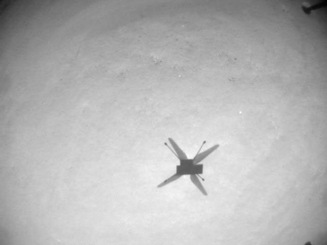 This is a black and white image of the Ingenuity Mars Helicopter. The camera is directed downwards to track the ground during flight.