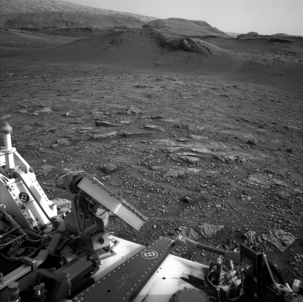 Black and white image of Mars, with parts of the Curiosity rover visible