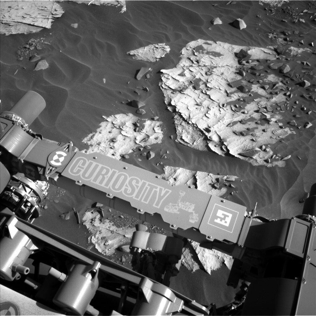 This is a black and white image of the smooth, sandy surface of Mars. There are large rough boulders embedded in the sand with smaller rocks scattered around.