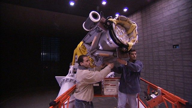 This image shows two engineers aiming the cannon that will fire the tightly packed parachute into the wind tunnel.