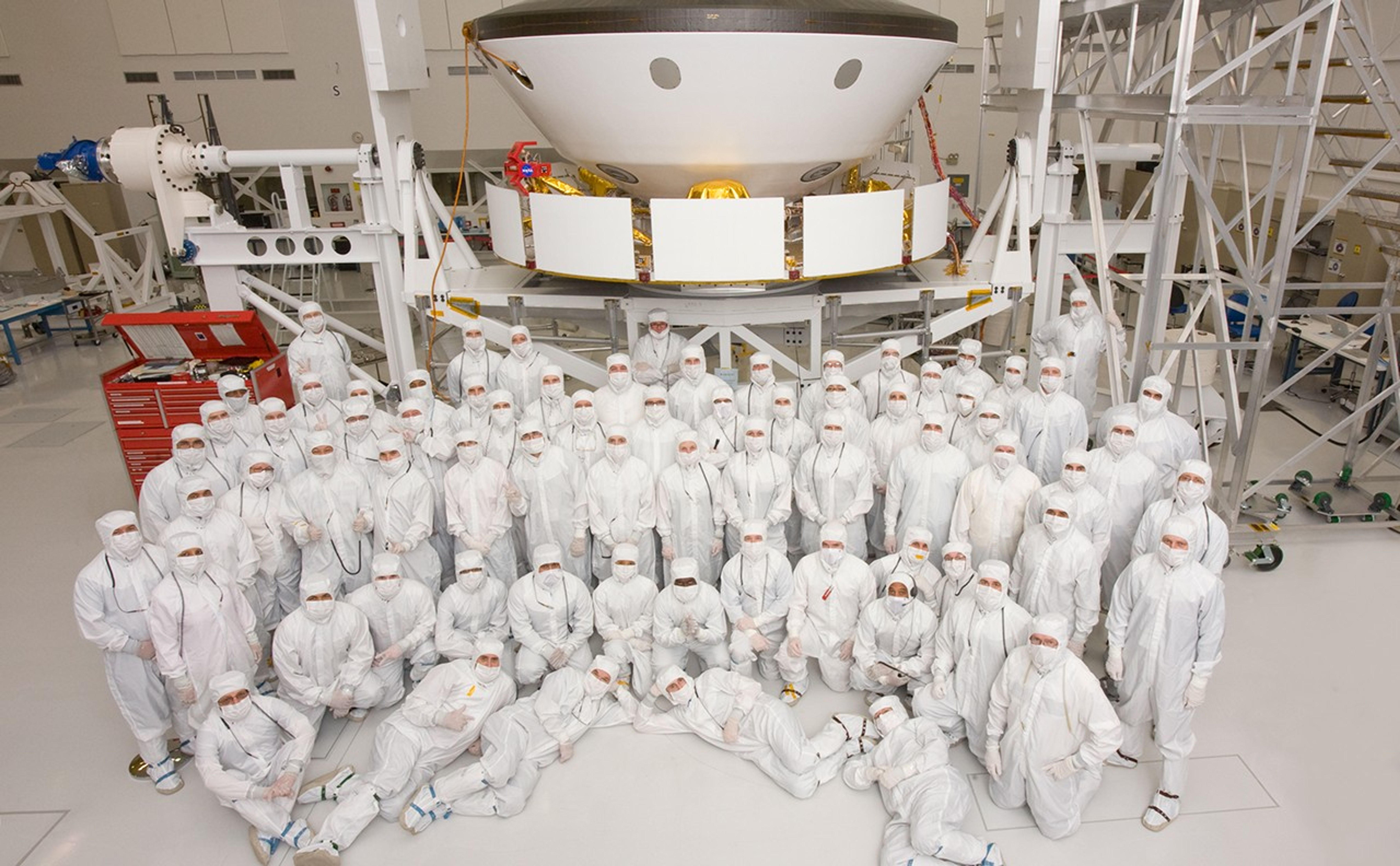 This photo shows 70 members of the Mars Science Laboratory team in Jet Propulsion Laboratory's Spacecraft Assembly Facility after they have prepared the spacecraft to go to a different area for the environmental tests. The team members are dressed in "bunny suits" (white protective gear) and are positioned in various poses in front of the spacecraft.