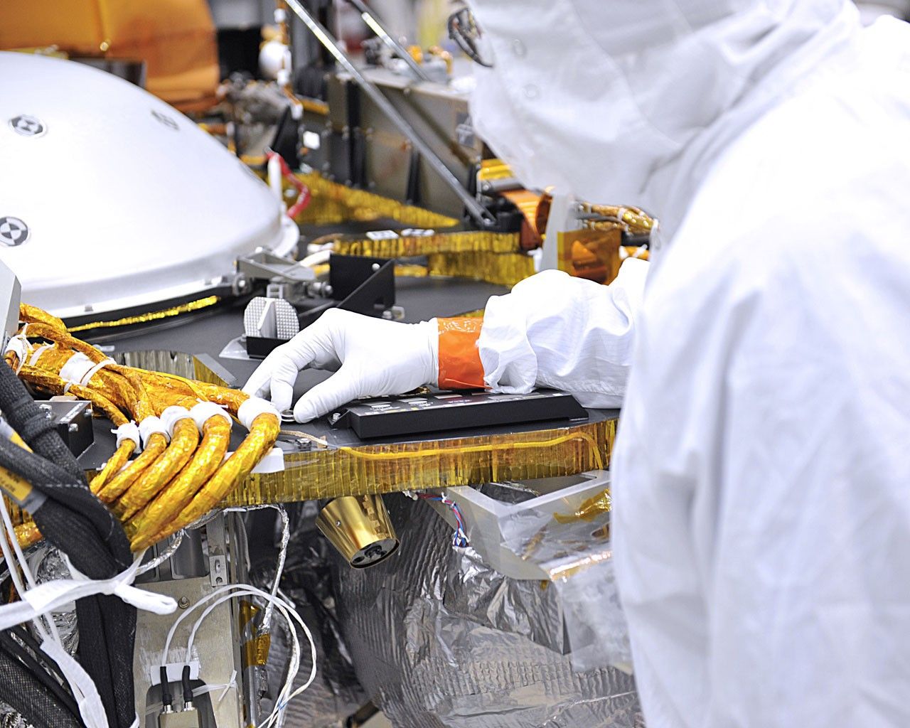 An engineer in the clean room at Lockheed Martin Space in Littleton, Colorado, affixes a dime-size chip onto the lander deck of NASA's InSight spacecraft.