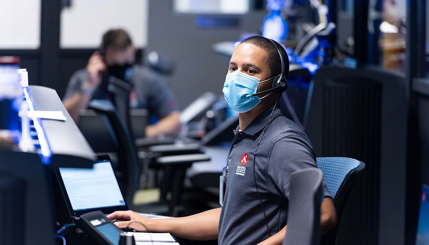 Engineer wearing mask looking across room in mission control