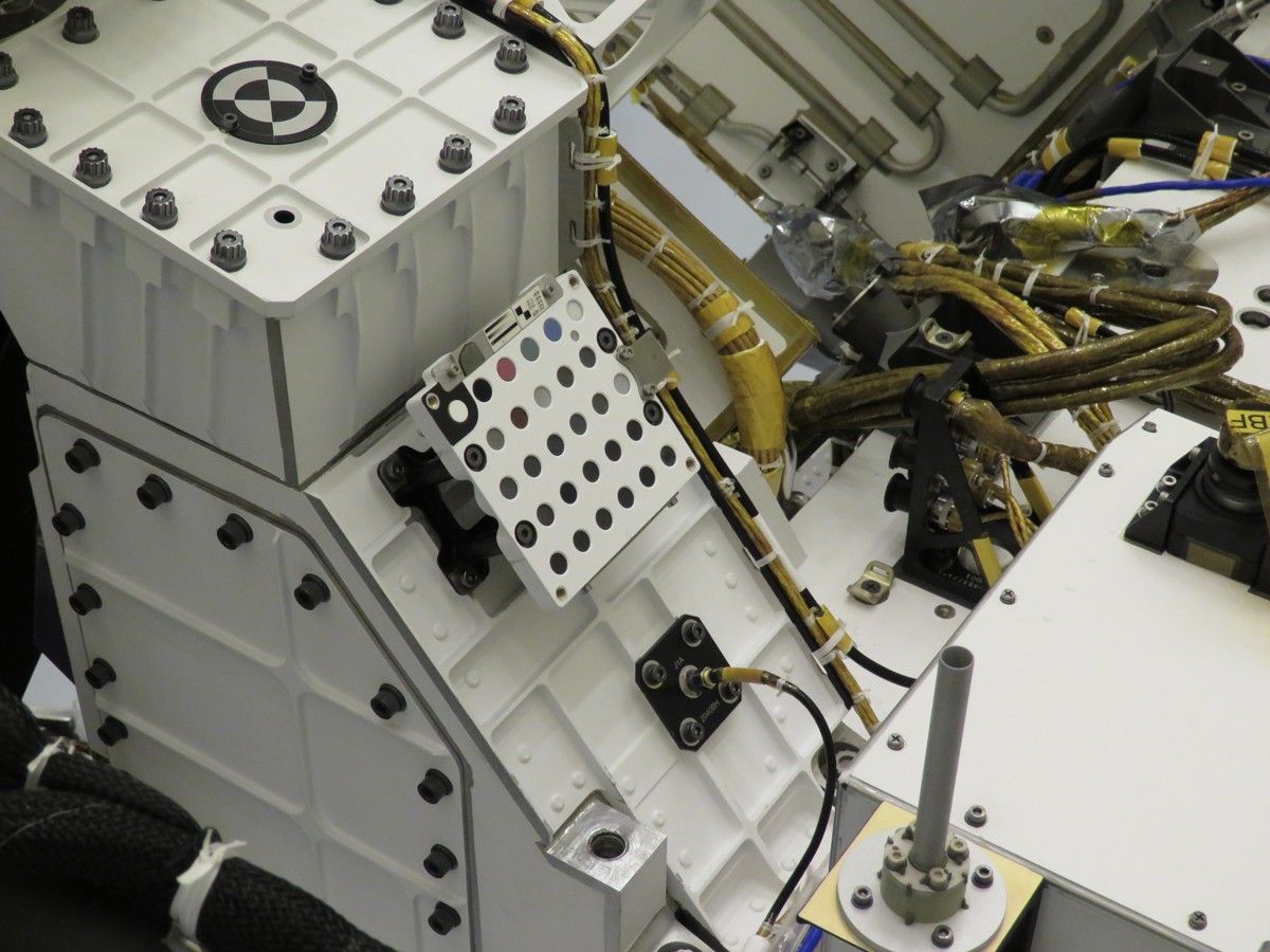A white, square unit with rows of small color and grayscale dots attached to the top of the Perseverance rover.