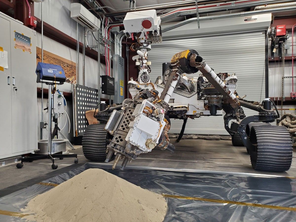 Optimism, a full-scale replica of NASA’s Perseverance Mars rover, tests a model of Perseverance’s regolith bit in a pile of simulated regolith – broken rock and dust – at JPL.